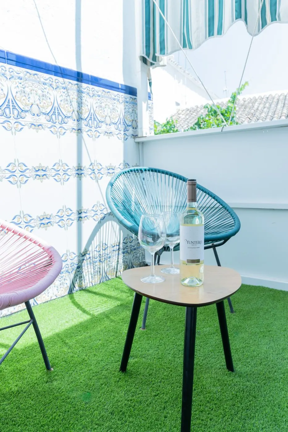 Rincón de la terraza con azulejos, sillas de colores y una botella de vino